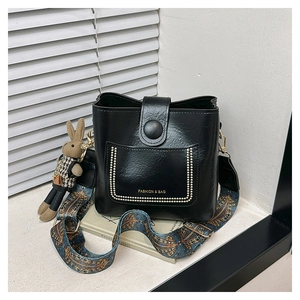 Detail of black glossy bucket bag with ethnic patterned wide strap and rabbit charm