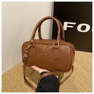 Detailed close-up of brown Boston bag with embossed lettering and golden hardware