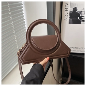 Detail of dark brown geometric handbag featuring a large circular handle and gold hardware