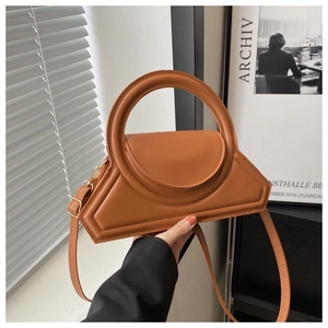 Detail of caramel leather handbag featuring a unique geometric shape and round top handle