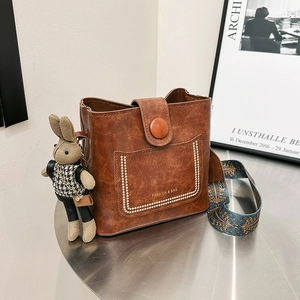 Brown faux leather bucket bag with printed wide shoulder strap and rabbit charm