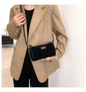 Détail du sac cylindrique noir avec logo doré sur fond de costume beige élégant