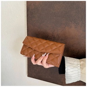 Close-up of model holding quilted deep brown long wallet with elegant diamond pattern