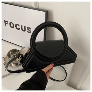 Detail of a minimalist black geometric handbag with a large gold ring handle and leather strap