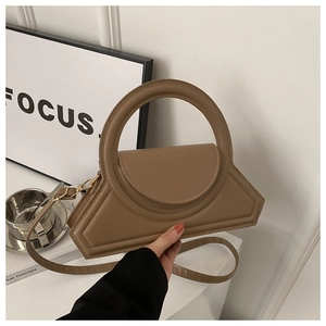 Detail of tan geometric handbag featuring a large round handle and smooth faux leather