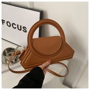 Close-up of caramel brown geometric handbag with oversized circular handle and crossbody strap