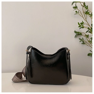 Détail d'un sac seau noir brillant avec une large bandoulière à chevrons chic