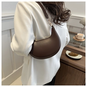 Sac hobo marron foncé porté à l'épaule sur un blazer blanc style minimaliste chic