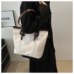 Detail of large canvas tote bag with brown leather handles and vintage metal buckle strap