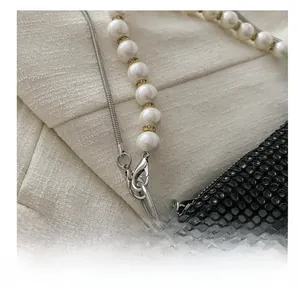 Detailed view of silver lobster clasp with pearl and snake chain on black rhinestone bag