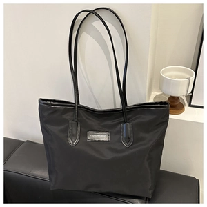 Detail of black nylon tote bag with leather straps and central fashion logo patch