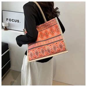 Shoulder shot of a large jute tote bag with orange ethnic geometric patterns and texture