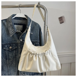 Détail du sac cabas en cuir blanc plissé suspendu à côté d'une veste en jean