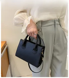 Detail of a minimalist black square handbag with sturdy top handles and metallic hardware