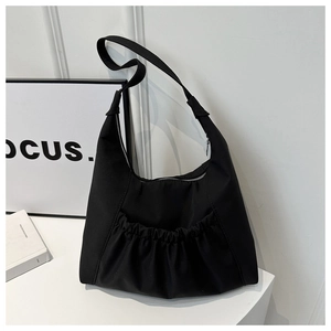 Détail du sac hobo en nylon noir avec poches plissées à l'avant et large bandoulière