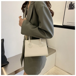 Detail of white minimalist crossbody bag with gold chain strap worn with a green suit