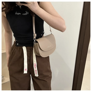 Selfie miroir montrant un sac selle en cuir mat beige avec bandoulière réglable de luxe