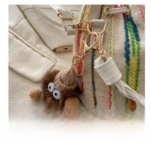 Close-up of a brown fuzzy monster bag charm with a knitted hat on a canvas tote bag