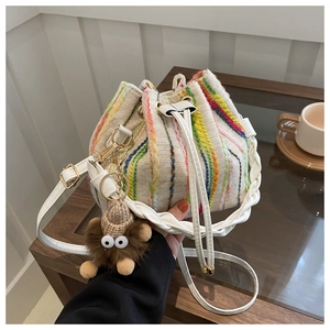 Detail of cream bucket bag featuring colorful vertical embroidery and plush charm