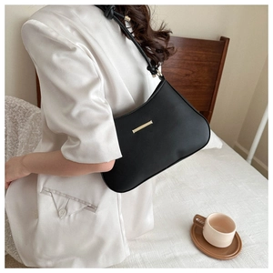 Borsa a spalla nera minimalista con dettaglio dorato su un elegante blazer bianco