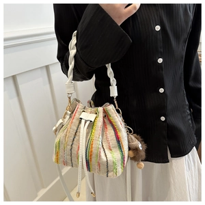Detail view of woven striped bucket bag with drawstring closure and plush pendant
