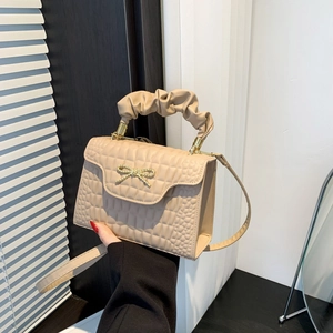 Beige quilted handbag with golden bow buckle and pleated handle shown in hand