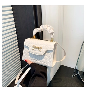 Detail of white crocodile embossed shoulder bag with golden bow and ruffled handle