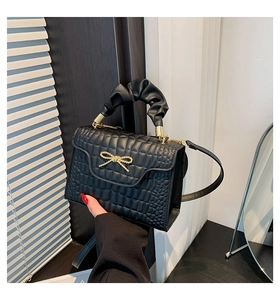 Close-up of black embossed square handbag with gold bow buckle and ruffled handle
