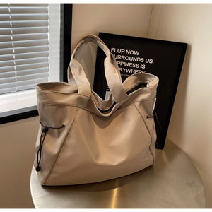 Detail of a beige canvas tote bag with black side drawstrings on a metallic table