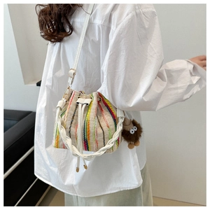 Detailed side view of canvas bucket bag with colorful stripes and plush monster charm