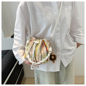 Detail of a beige woven bucket bag with rainbow stitching and brown plush charm