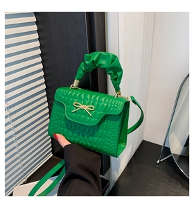 Close-up of bright green quilted handbag with gold bow lock and ruched handle