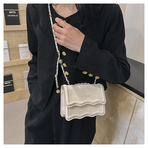 Detail of a wave-shaped flap crossbody bag in creamy finish with chain strap