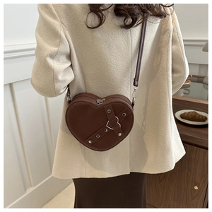 Sac bandoulière marron en forme de cœur avec clous porté sur un manteau en tweed beige