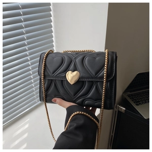 Detail of black quilted crossbody bag with gold heart-shaped lock and chain strap