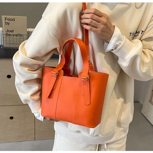 Détail d'un cabas orange vif avec bandoulière réglable porté par un mannequin en scène