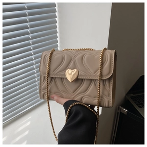 Close-up of heart-shaped quilted pattern and golden heart twist lock on beige handbag