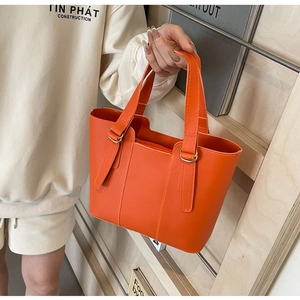 Détail d'un sac cabas orange vif en cuir avec anneaux dorés et doubles poignées