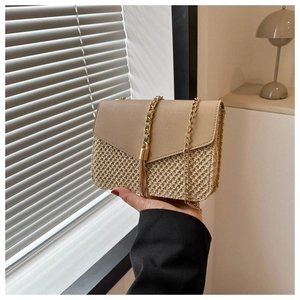 Detail of hand-held straw crossbody bag with golden chain strap and fringe tassel