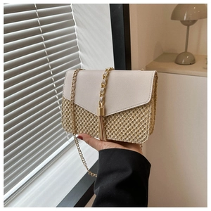 Detailed view of straw-woven crossbody bag featuring golden chain strap and tassel