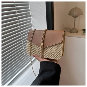 Detail of woven straw shoulder bag featuring brown leather flap and golden tassel