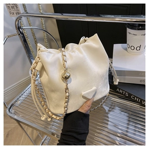 Detailed view of white drawstring bucket bag with gold chain and metal fashion plate