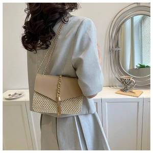 Detail of straw woven crossbody bag featuring beige leather flap and gold tassel accent