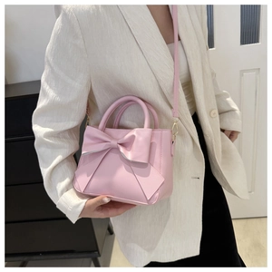 Close-up of pink bow square handbag with gold hardware on white blazer outfit