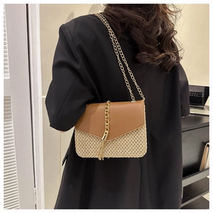 Detail of straw woven crossbody bag with brown leather flap and gold chain tassel
