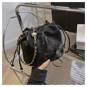 Detail of black drawstring bucket bag with gold hollow charm and woven chain strap