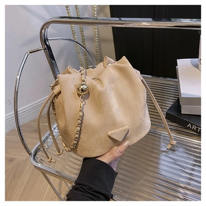 Detail of beige drawstring bucket bag featuring gold chain and FASHION leather patch