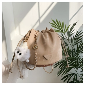Detail of beige drawstring bucket bag with gold chain strap and fluffy white charm