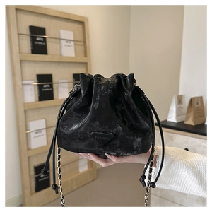Detailed view of black matte leather bucket bag with gold chain and fashion emblem