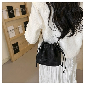 Detail of a black drawstring bucket bag with a chain strap worn by a model in white
